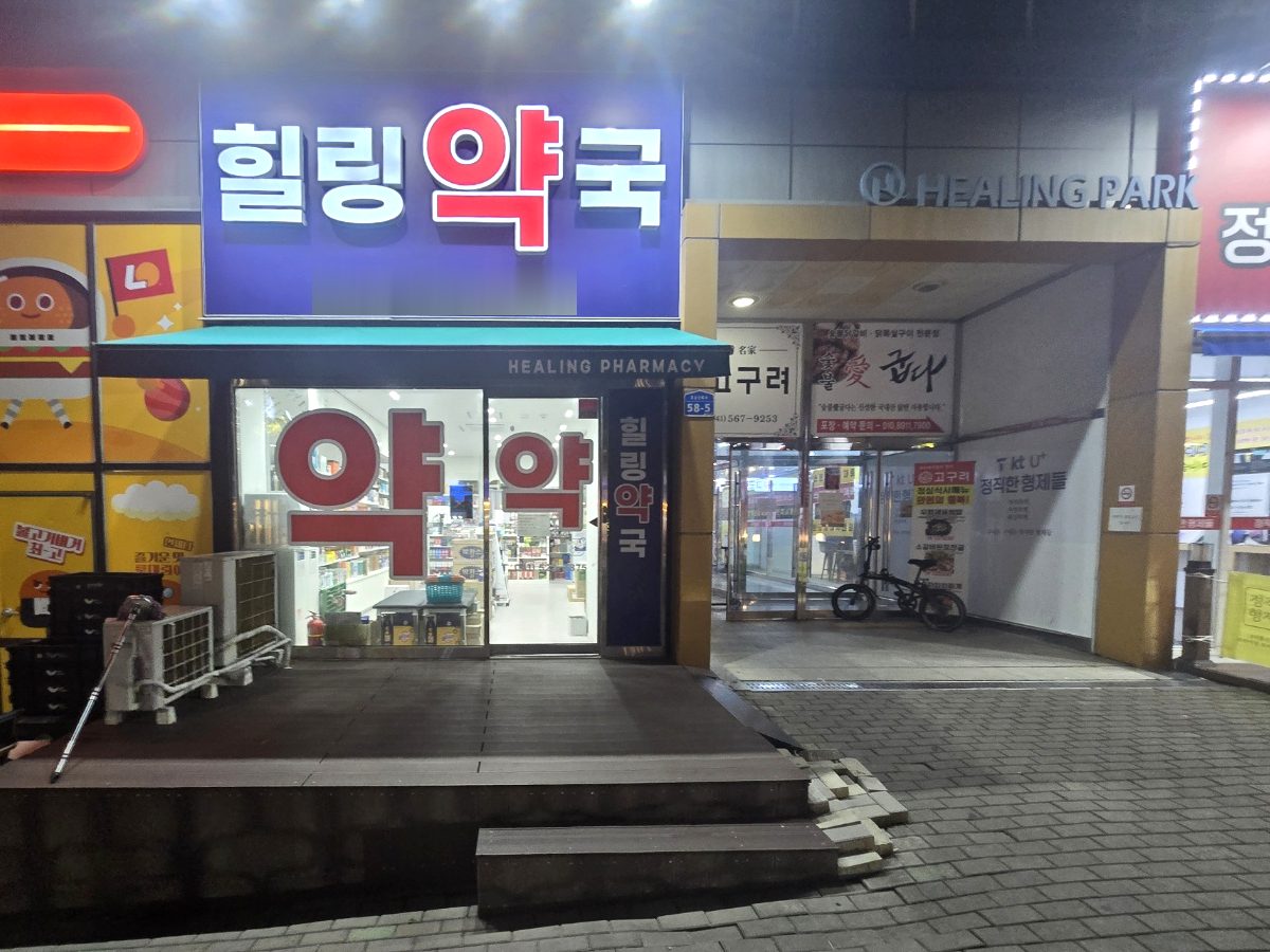 힐링약국 외관. 파란 간판, 힐링파크 건물 입구 옆